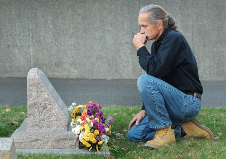 Man kneeling in front of grave with fresh flowers after losing a loved one to a serious pool injury